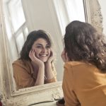 Image of woman looking at herself in the mirror. By Andrea Piacquadio for Pexels