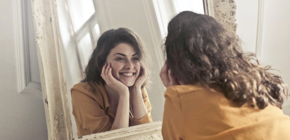 Image of woman looking at herself in the mirror. By Andrea Piacquadio for Pexels